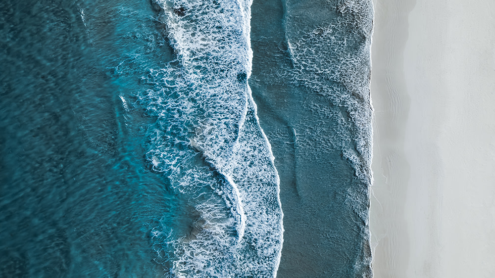 aerial view of waves breaking against white sand beach