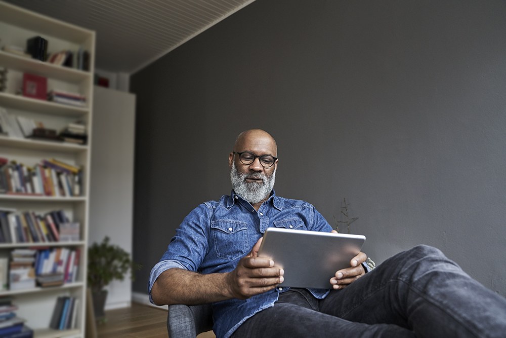 midaged black man reading on his tablet at home