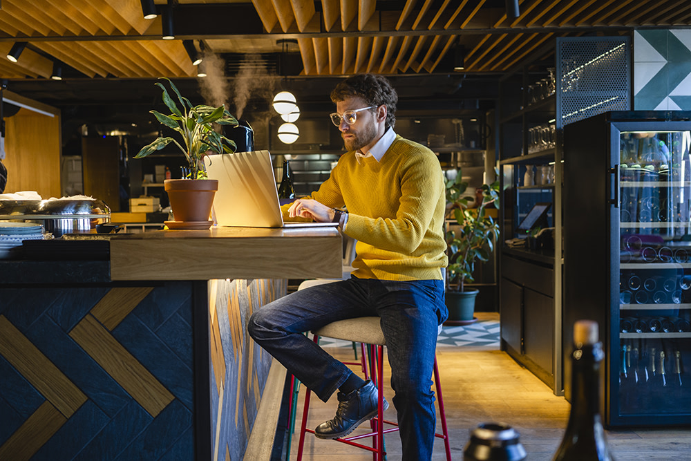 white man with beard in a yellow sweater working alone at a coworking space