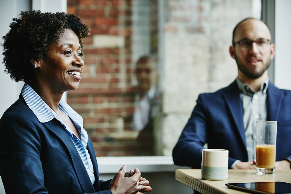 Black woman and white man in navy blazers sitting at a table together