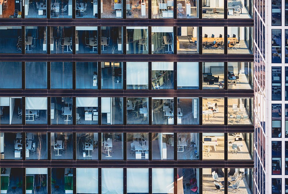 Exterior side view of multiple levels of an office building, showing various office rooms through the windows