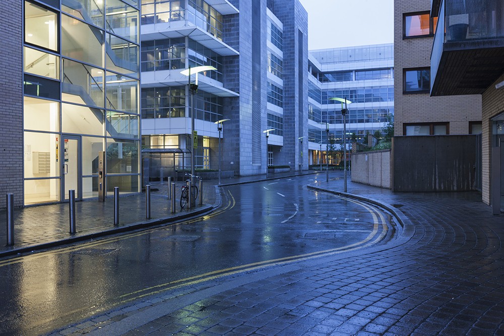 Early morning view of an empty, wet, single lane road and the neighboring commercial buildings