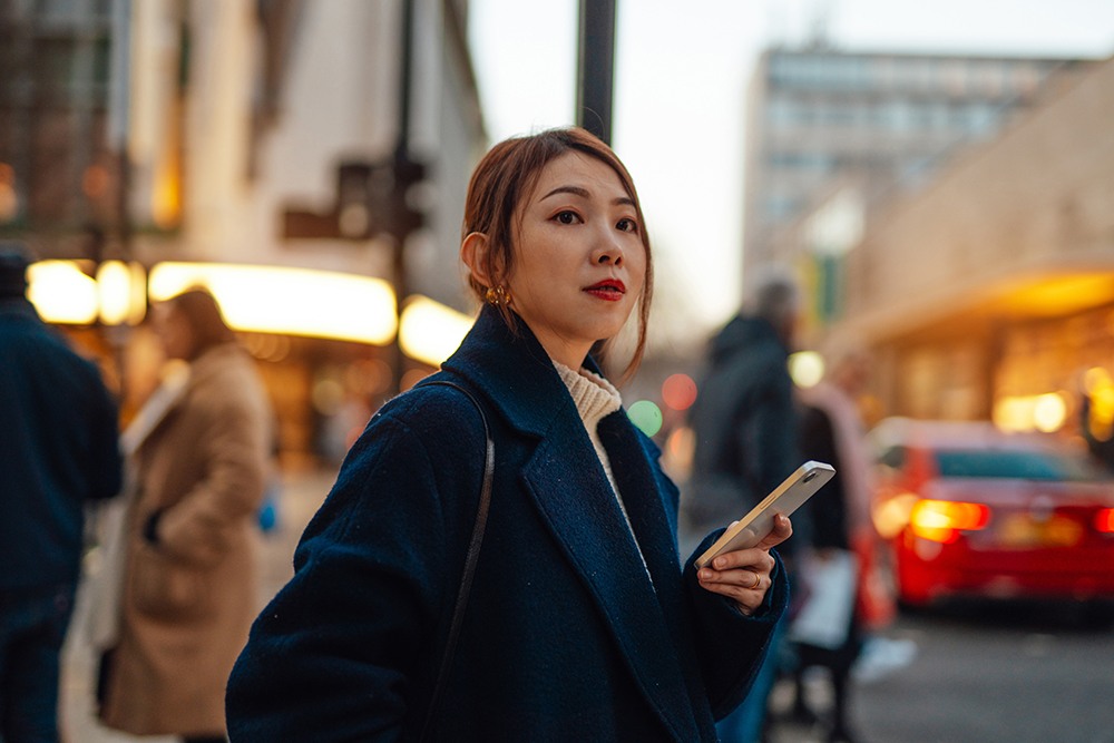 Asian woman in navy jacket, waiting for a taxi in the city