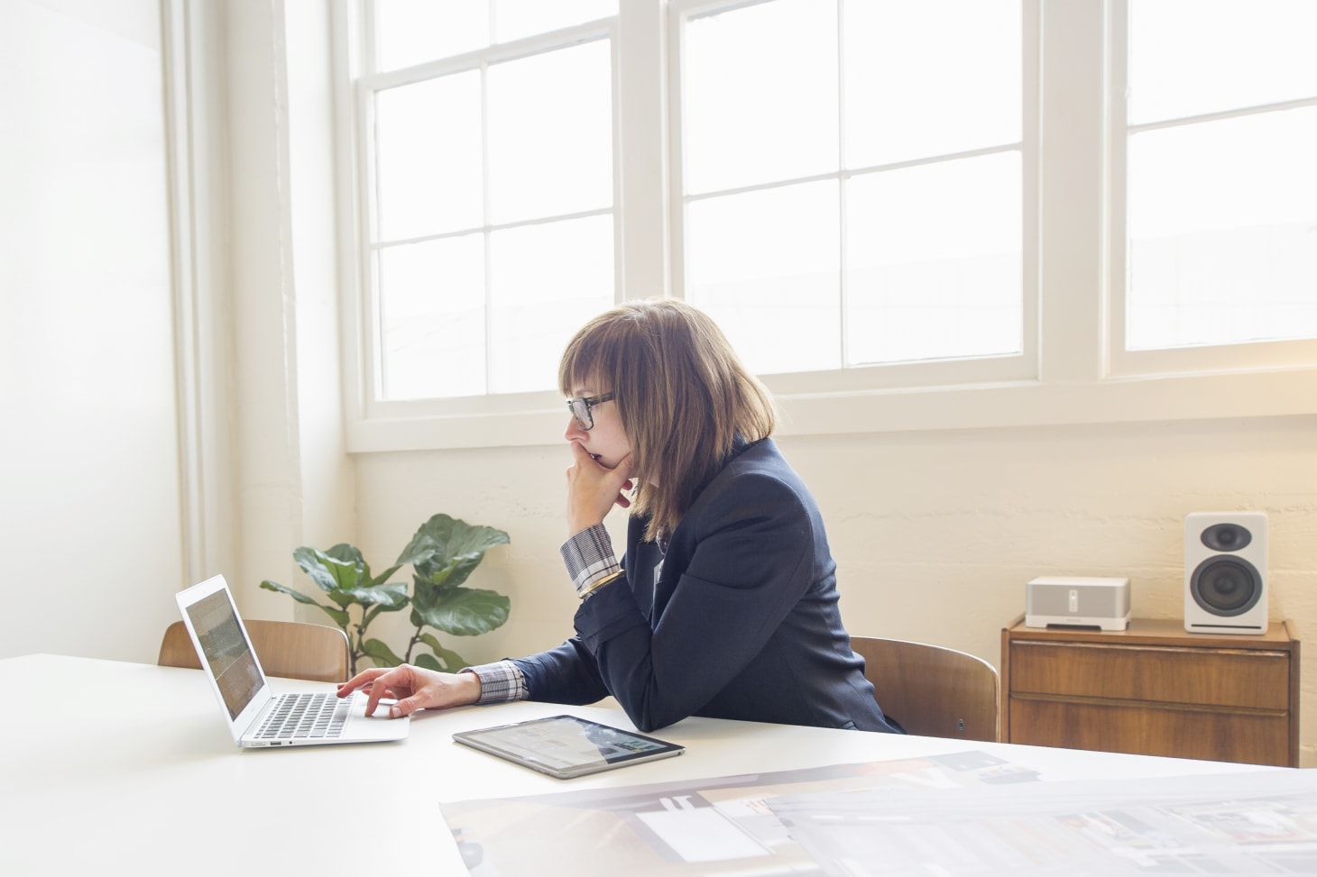 white woman with brown short hair and bangs, wearing a suit jacket and working on her laptop