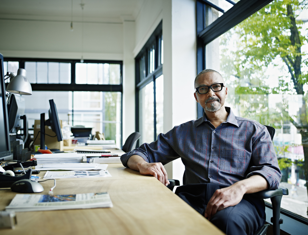 middle aged black man sitting at modern desk in team office next to window