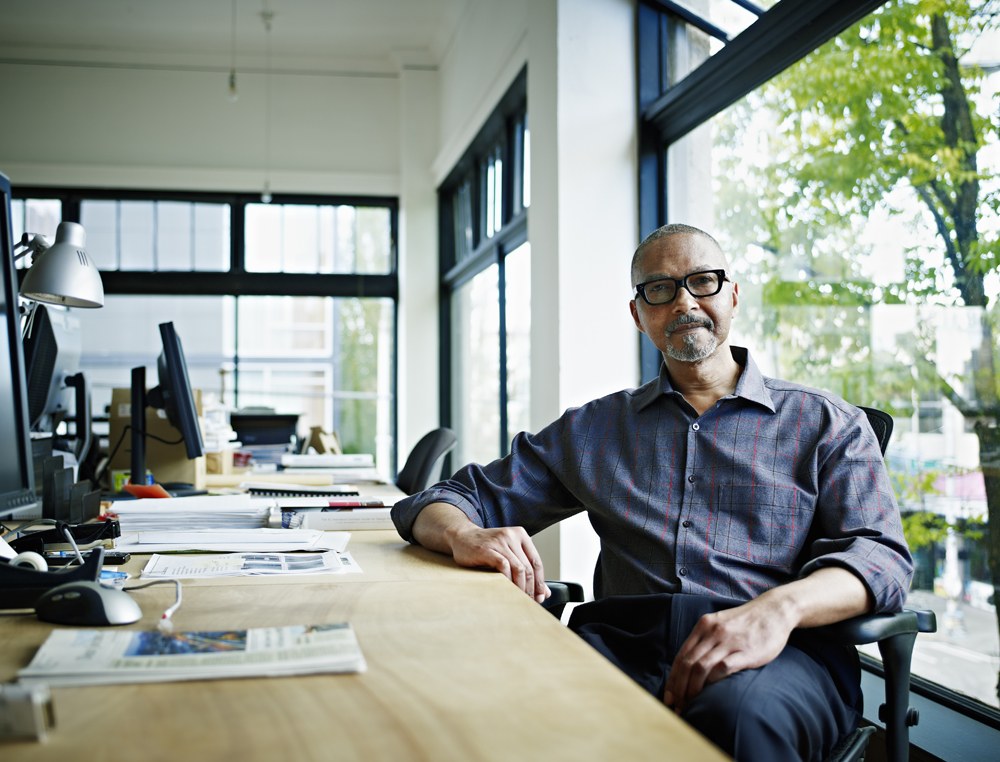 Man in glasses sitting at long desk in front of window