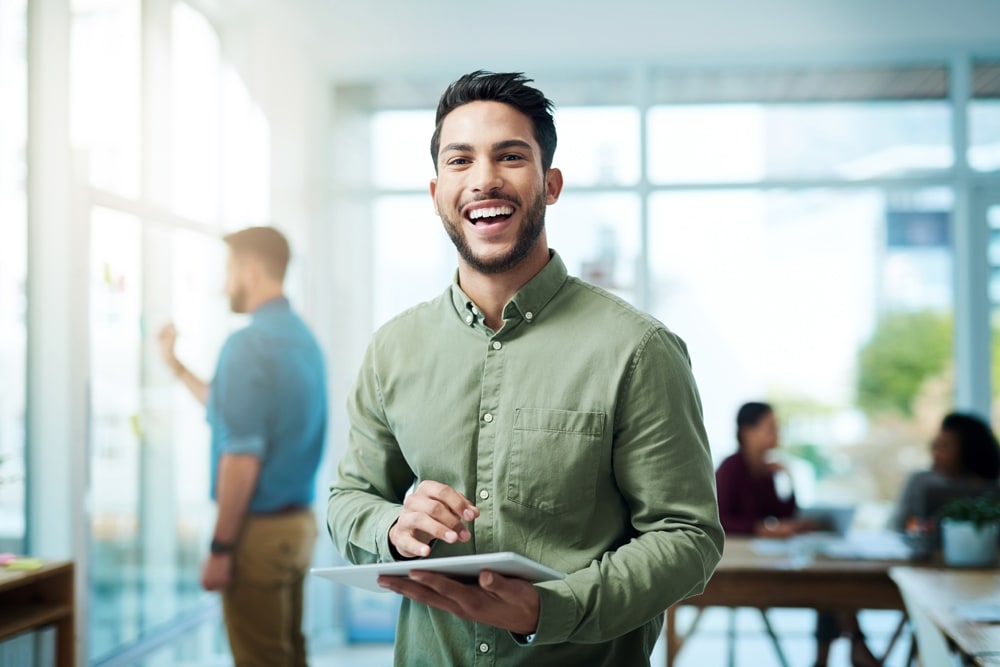 Man in green smiling holding tablet