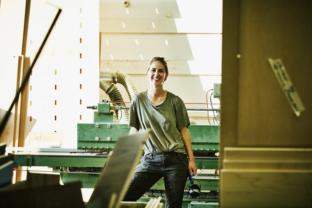 blonde woman in green shirt and jeans working in a workshop