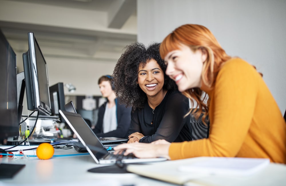 two female coworkers chatting at a shared workstation