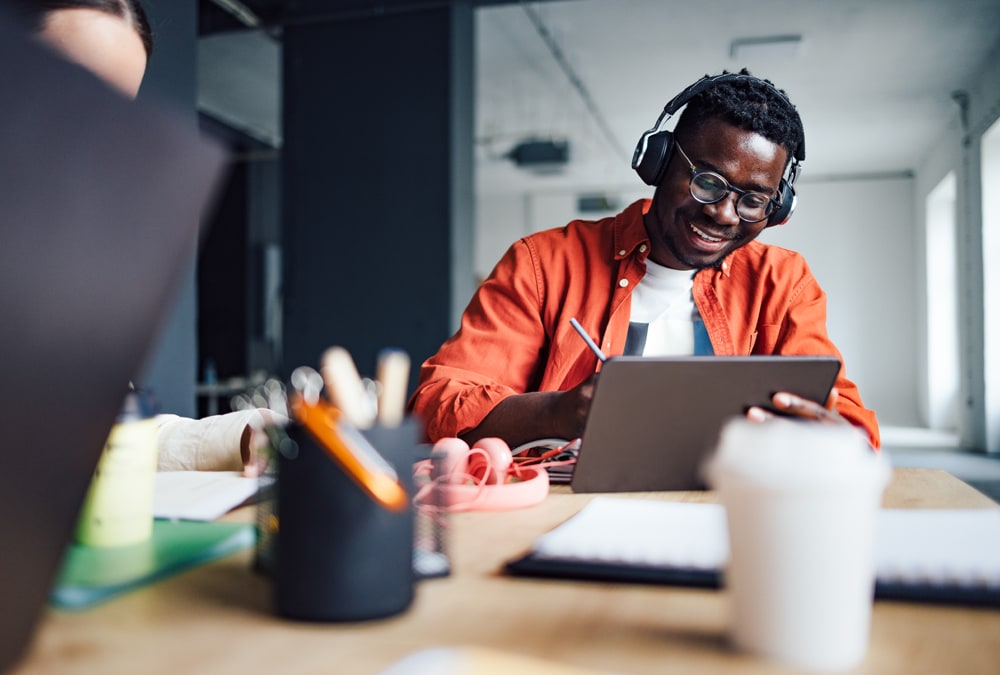 young Black man in orange shirt listening to music while working