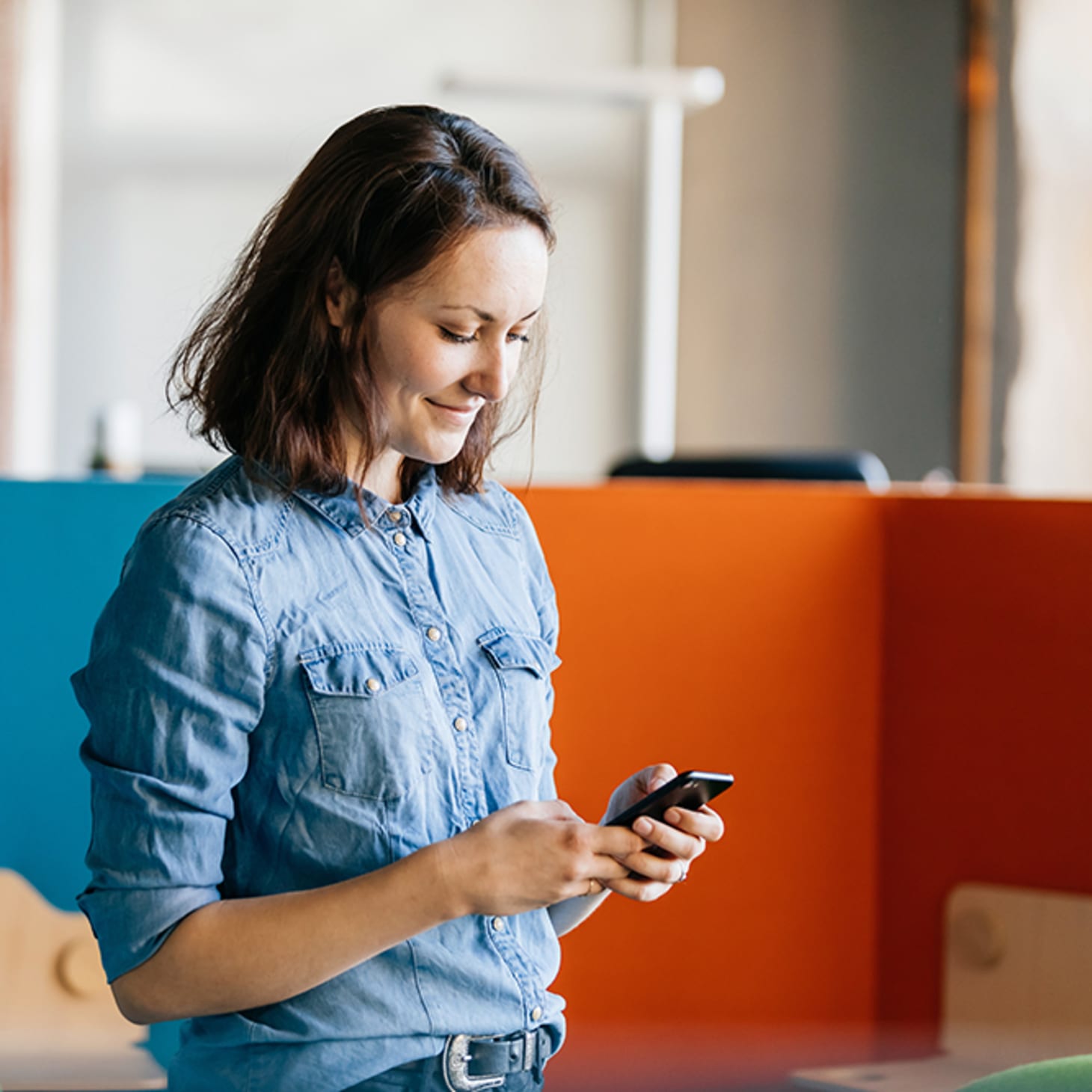 white woman in denim shirt texting on her cell phone