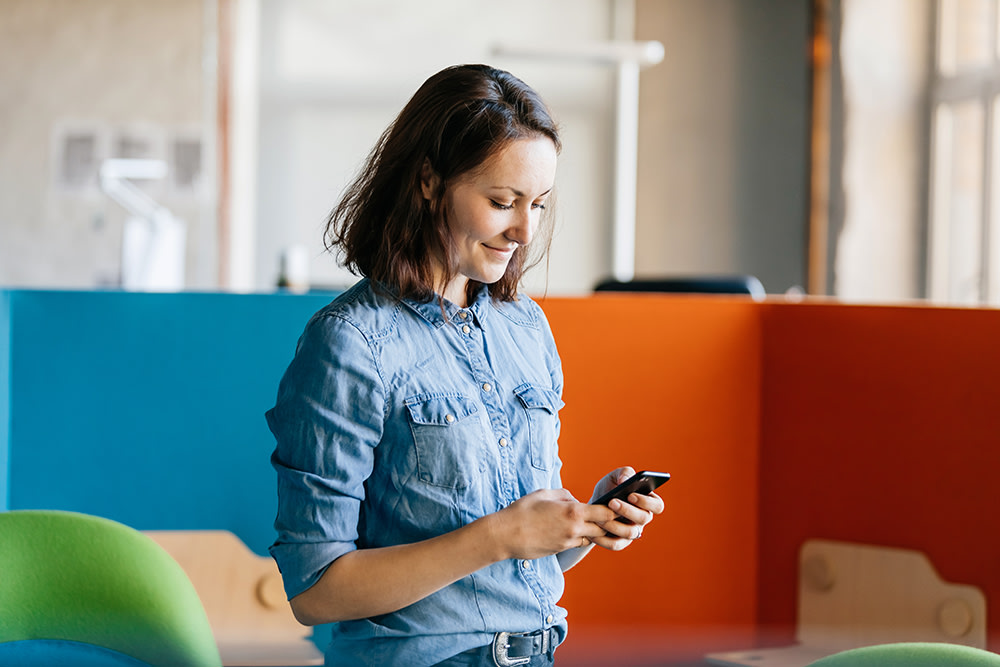 white woman texting on her phone in front of brightly colored office furniture