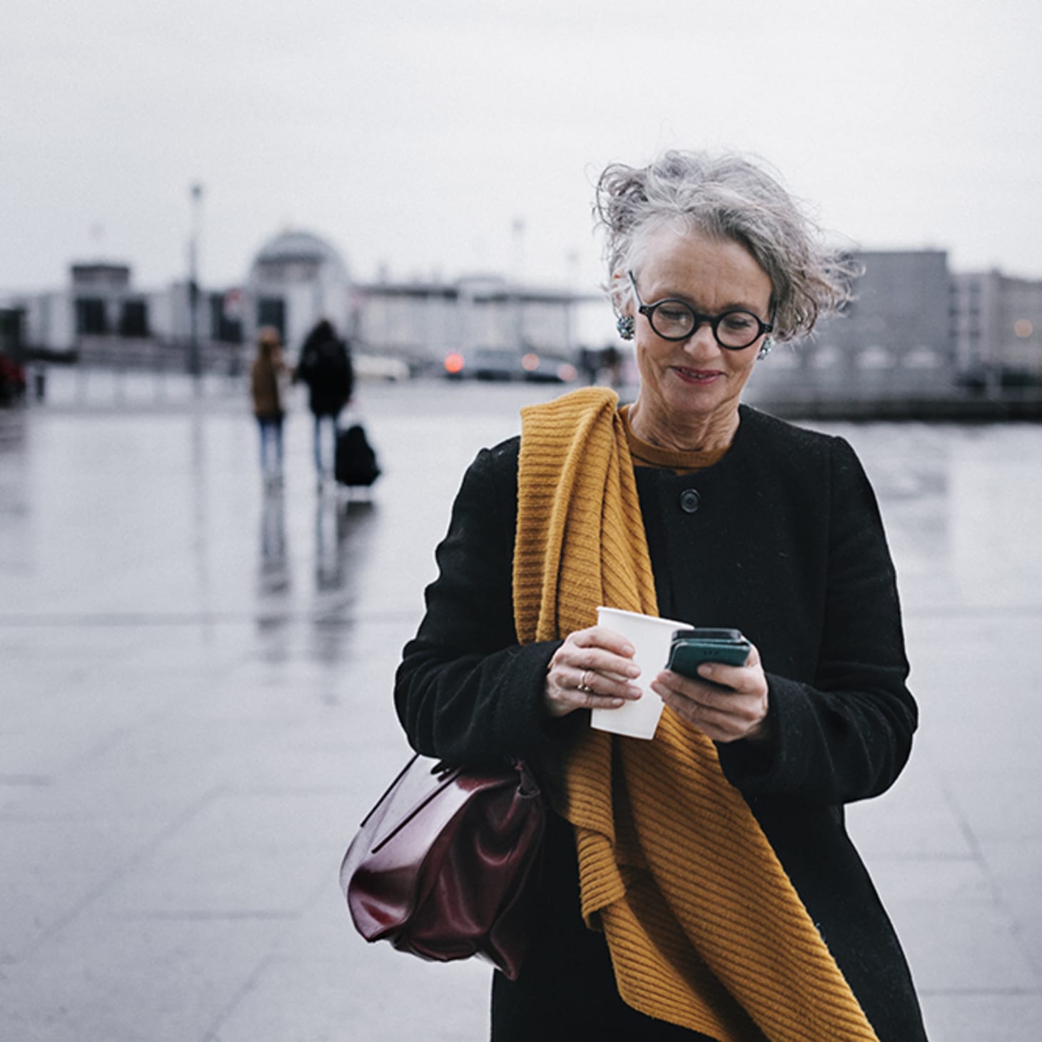 midaged white woman walking in a plaza, looking at her phone