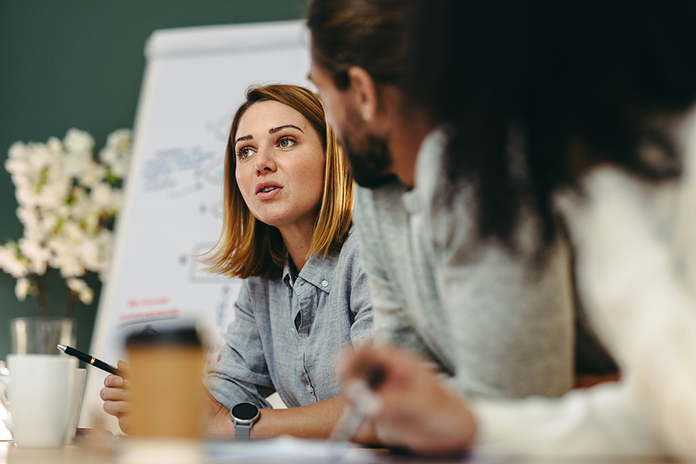 white woman with short blonde hair talking at team table meeting