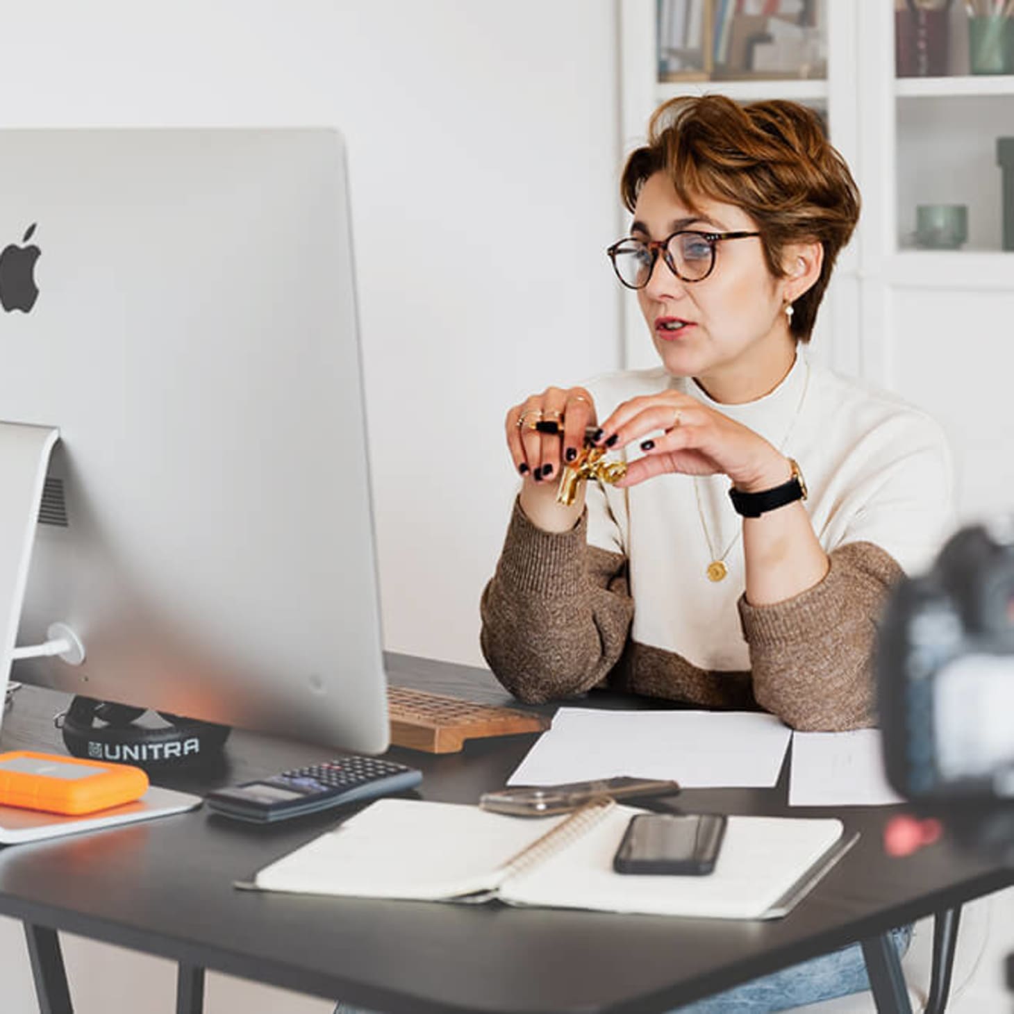 white woman with short hair and glasses, on a video conference call at home office