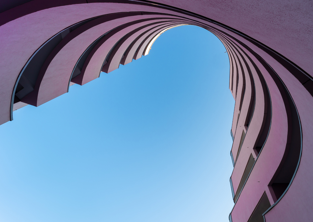 vertical view of tiered building curving inward against clear blue sky