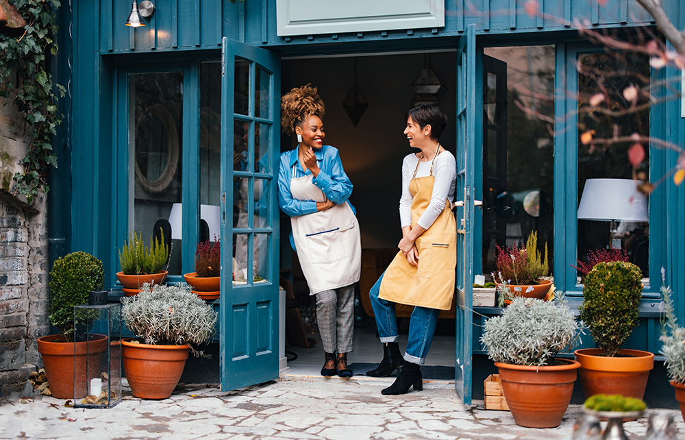 female small business coworkers chatting outside the shop door wearing aprons