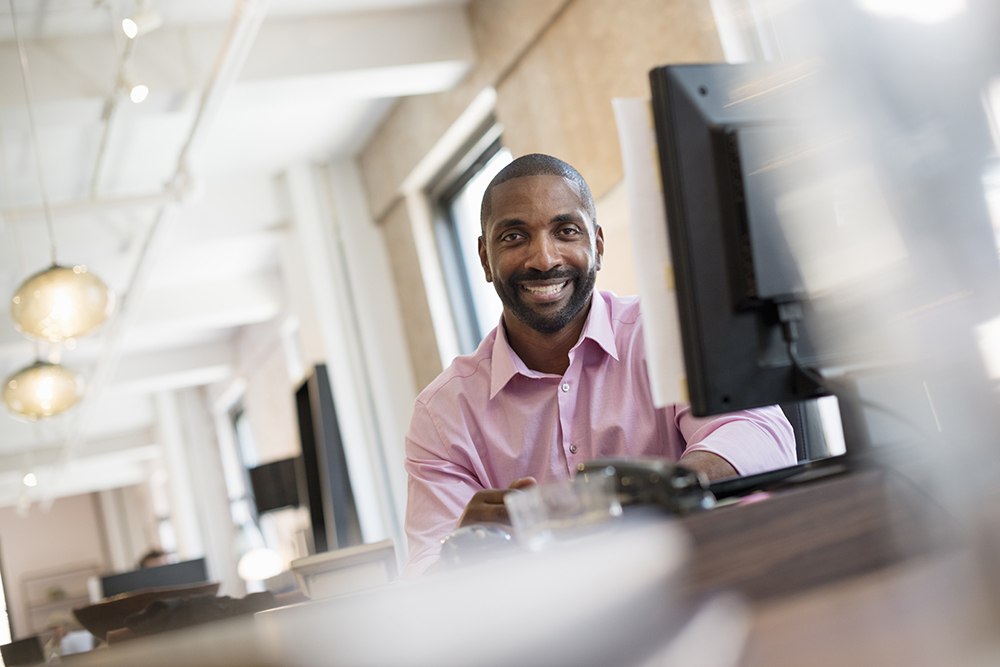 Black man in pink shirt smiling at his computer desk