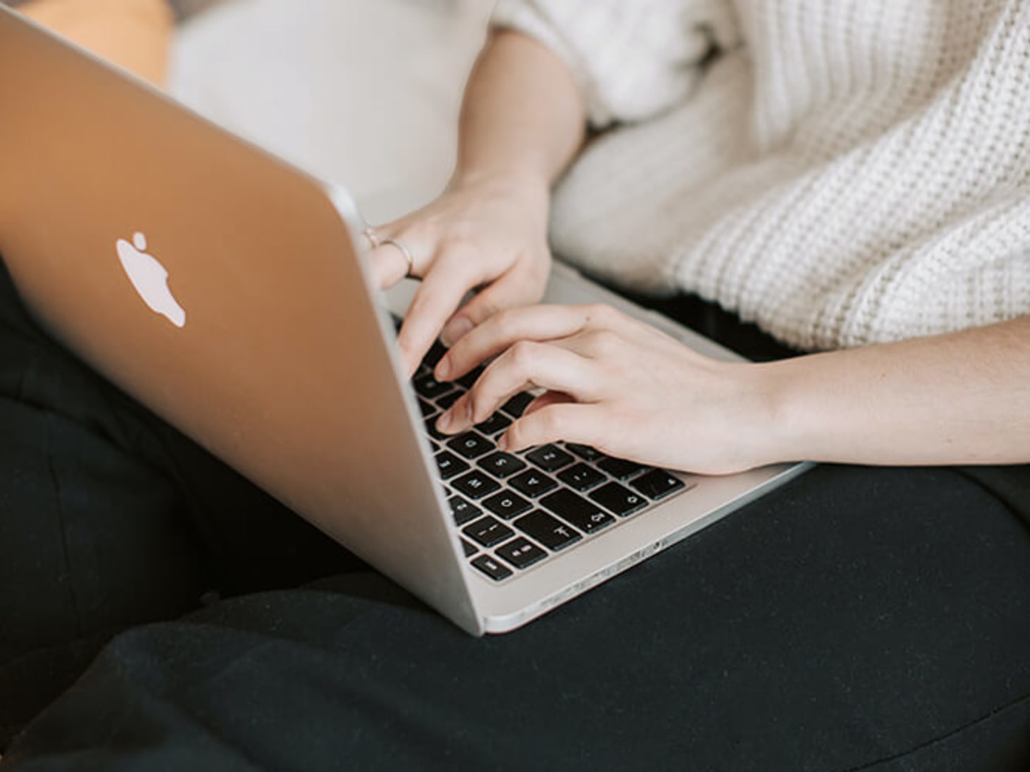 person in sweater typing on Apple laptop
