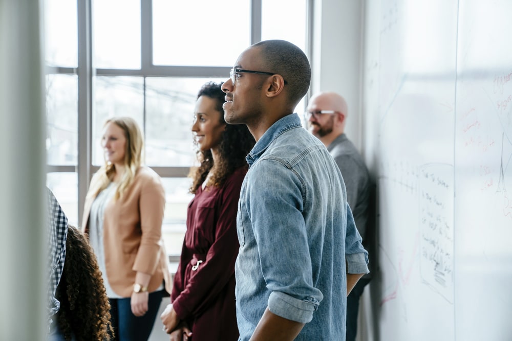 team standing in a meeting with a whiteboard behind them