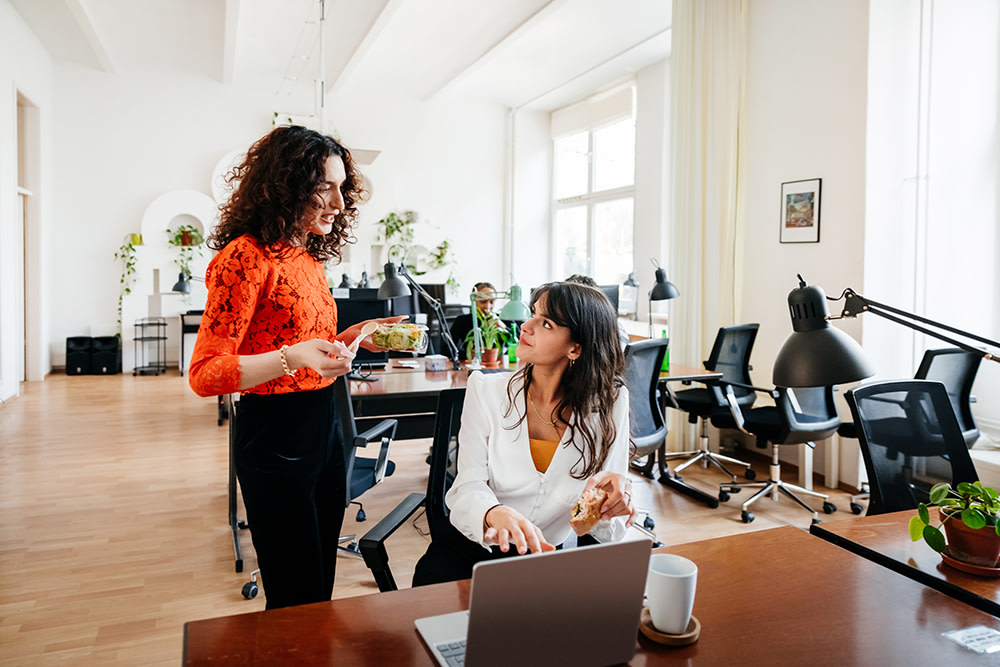 two female colleagues chatting over lunch at the office